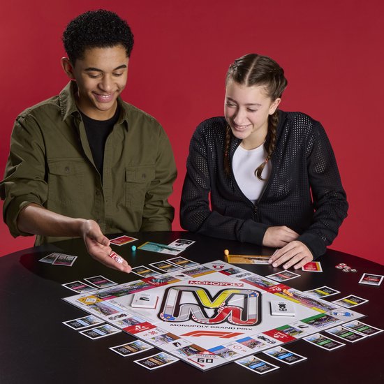 Twee kinderen kijken lachend naar dobbelstenen. Een Monopoly Grand Prix bordspel ligt op tafel.