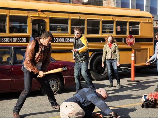 Man met honkbalknuppel in gevecht met zombies bij een schoolbus.