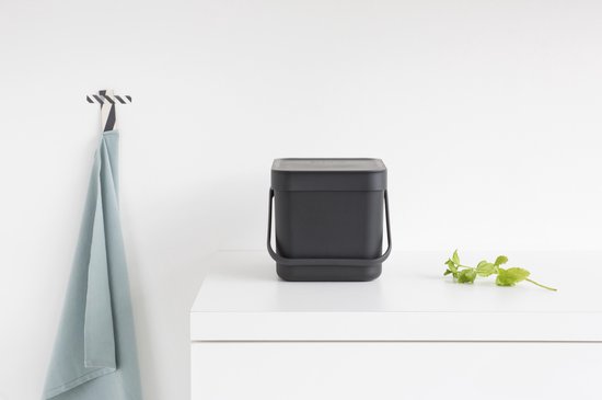 Boîte à compost Brabantia gris foncé avec couvercle sur un plan de travail blanc.
