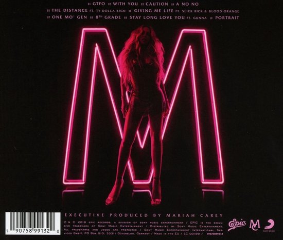 Mariah Carey staat voor een grote neon 'M'. Ze draagt een zwarte jurk, hoge hakken en heeft lang blond haar.