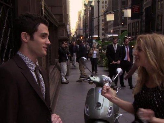 Man in bruin pak en vrouw in zwart met scooter op straat in New York.