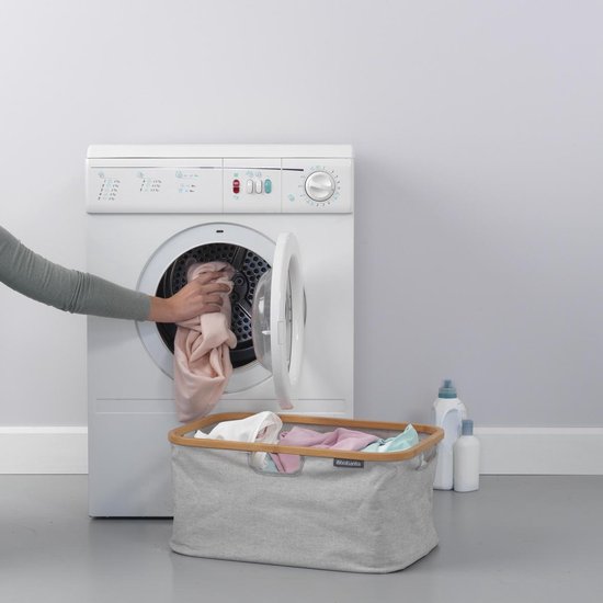 Grijze Brabantia wasmand naast een wasmachine met wasgoed.