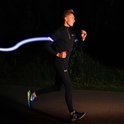Man in zwart trainingspak en blauwe hardloopschoenen met een blauw oplichtende armband om zijn arm.