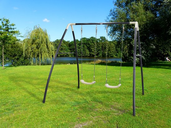 Une balançoire double en métal anthracite avec sièges crème, dans un parc près d'un lac.