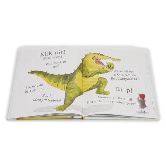 Een geopend kinderboek met een illustratie van een grote groene krokodil die letters eet. Tekst: 'Kijk uit! Wat doet-ie nu?'