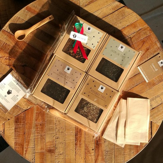 Cadeauset met vier soorten Arelo thee, houten lepel en papieren theefilters op een houten ondergrond.