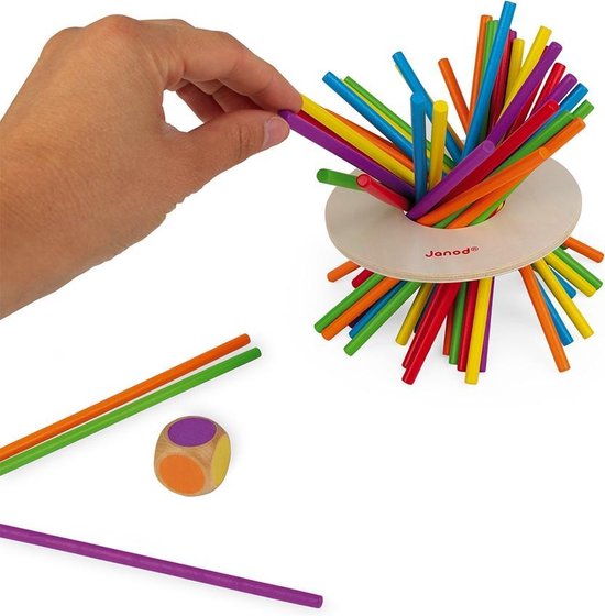 Hand trekt een kleurrijk stokje uit het spel "Crazy Sticks", met losse stokjes en dobbelsteen ernaast.