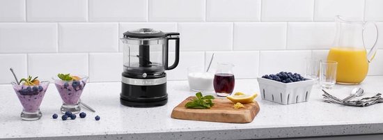 Zwarte KitchenAid hakmolen op aanrecht met kommetjes yoghurt, blauwe bessen en sinaasappelsap.