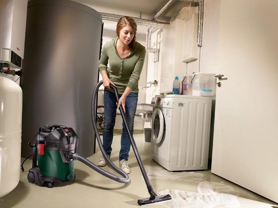 Vrouw met spijkerbroek gebruikt een groene en zwarte Bosch ketelstofzuiger in een bijkeuken met wasmachine.