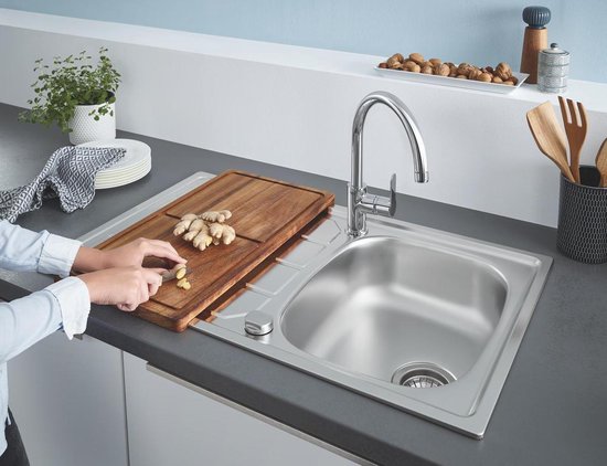 Chroomkleurige keukenkraan met gebogen hoge uitloop in een gootsteen met snijplank.