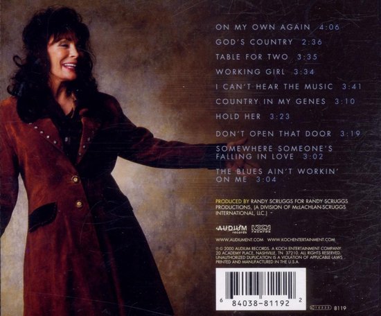 Loretta Lynn in bruine jas met gouden knopen, staand met de armen naar beneden.