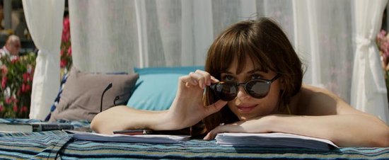 Vrouw met zonnebril, liggend op een bed met gestreepte kussens en boeken.