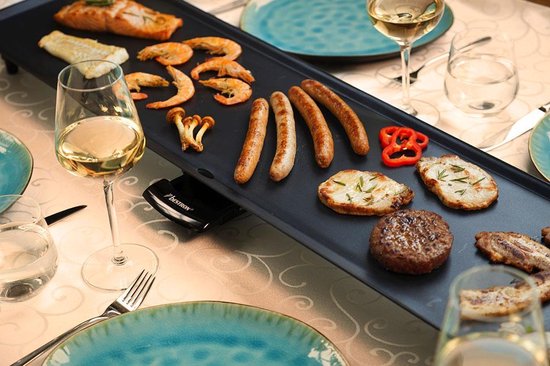 Gegrilde zalm, garnalen, worstjes, vlees en groenten op een bakplaat, met wijnglazen op de tafel.