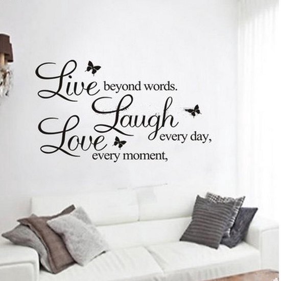 Sticker mural noir avec texte 'Live beyond words. Laugh every day, Love every moment.' et papillons, au-dessus d'un canapé blanc.