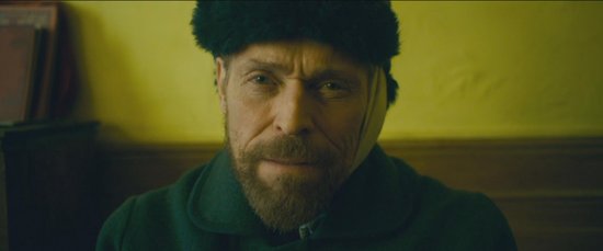 Close-up van Willem Dafoe als Vincent van Gogh, met een bontmuts en groene jas.