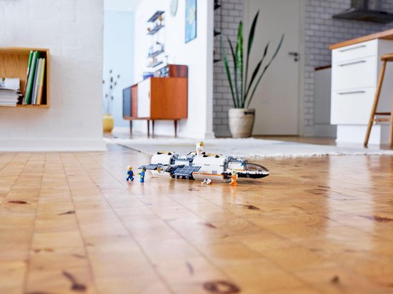 Wit LEGO ruimteschip met zonnepanelen en astronauten in een woonkamer op houten vloer.