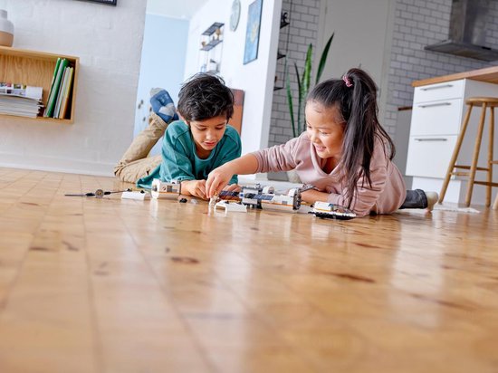 Twee kinderen spelen met LEGO-onderdelen op een houten vloer.