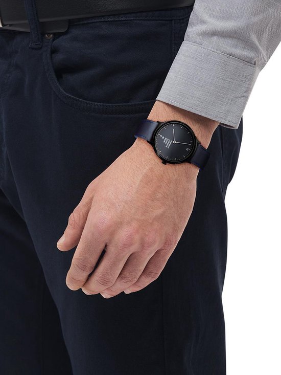 Man draagt een Mondaine horloge met zwarte wijzerplaat en donkerblauwe lederen band om de pols.