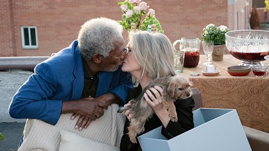 Morgan Freeman en Diane Keaton kussen op een dak, met een puppy en een gedekte tafel.
