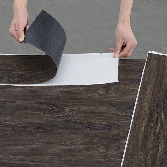 Handen die de beschermlaag van een donkerbruine PVC vloerplank met houtnerf verwijderen.