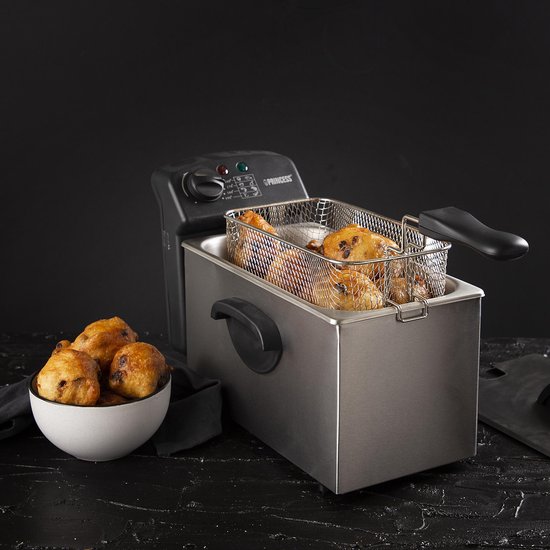 Roestvrijstalen frituurpan met mandje vol gefrituurde snacks en een kom met oliebollen.
