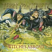 Illustratie van 'Witches Abroad' met drie heksen, een kat en een kikker in modderig water.