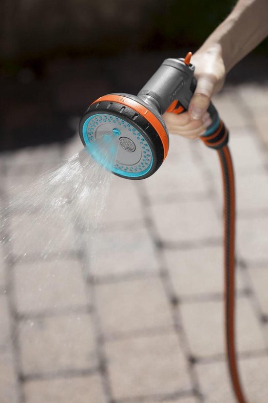 Grijze GARDENA spuit met oranje en blauwe accenten sproeit water op een betegeld pad.