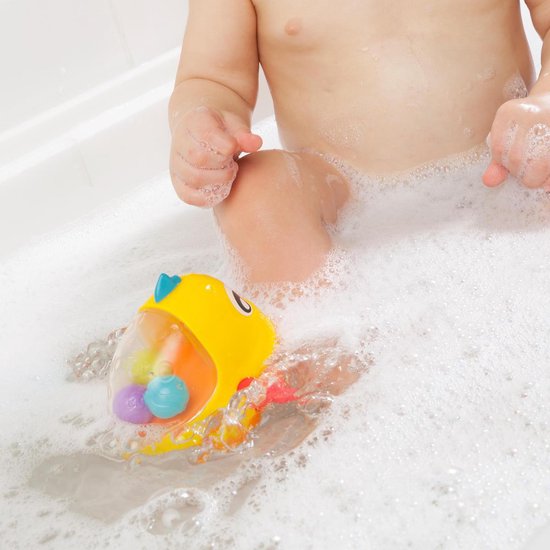 Een baby zit in een badkuip en speelt met een geel badeend visje met rode vinnen.