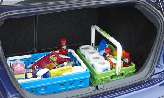 Blue and green folding crates filled with groceries, including toilet paper, bottles, and snacks, placed in a car boot.