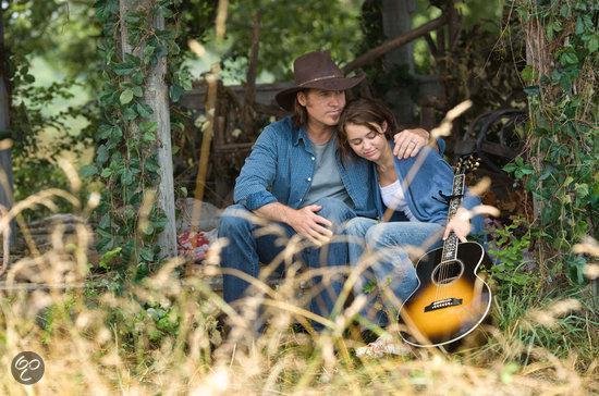 Miley Cyrus leunt op een man met een cowboyhoed en gitaar.