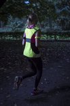 Vrouw in het donker joggend met een fluoriserend geel hesje met roze accenten en reflecterende strepen.
