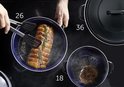 Een braadpan met een rollade op een kookplaat en een kleinere pan met een hamburger.