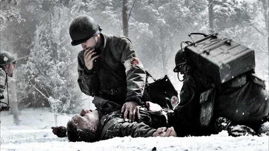 Twee militairen in de sneeuw, één helpt een liggende soldaat, beiden dragen uniformen en helmen.