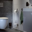 Une brosse de toilette avec un support foncé à côté d'une cuvette de toilette blanche, avec deux porte-rouleaux de papier toilette muraux.
