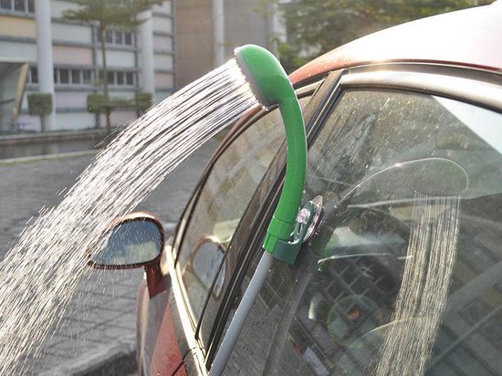 Groene draagbare douche met zuignap bevestigd aan de ruit van een rode auto, water spuitend.