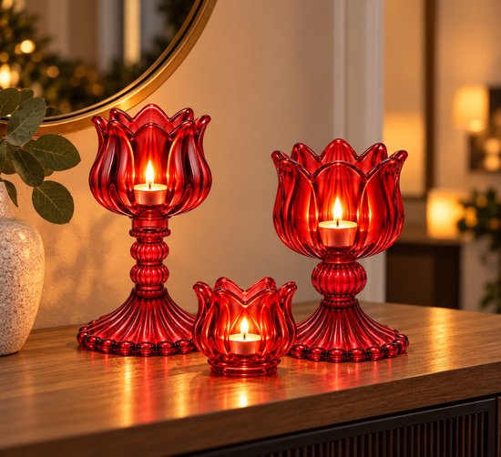 Set van drie rode glazen kandelaars en theelichthouders in bloemvorm, sfeervol verlicht op een houten tafel.