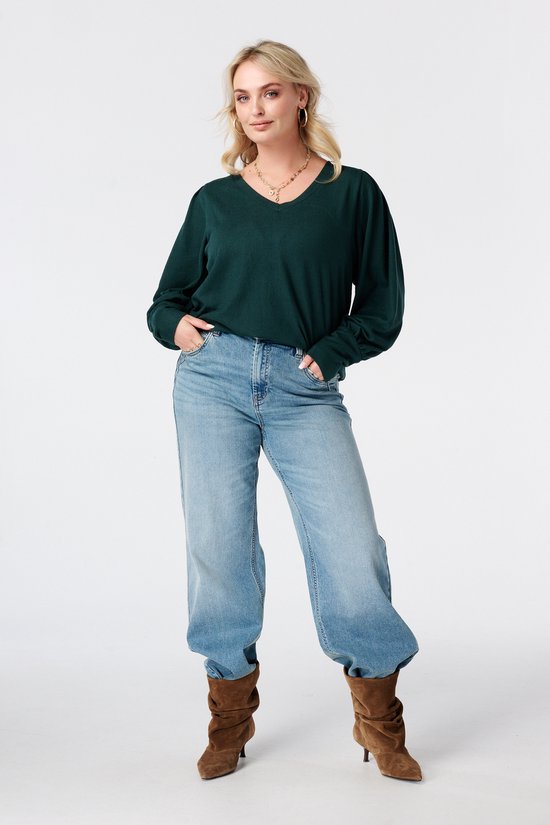Model in donkergroene top met pofmouwen, jeans en laarzen.