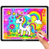 A3 lichtpad met een kleurrijke tekening van een eenhoorn, regenboog en sterren, met een hand die een stift vasthoudt.