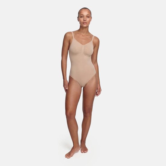 Model in een beige corrigerende bodysuit met dunne bandjes, volledig zichtbaar van top tot teen.