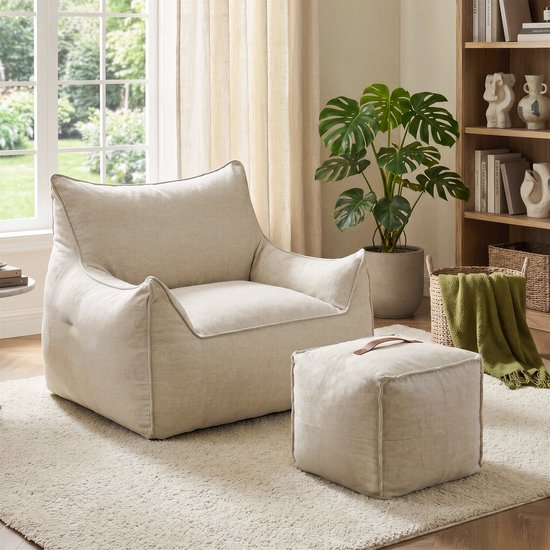 Beige zitzakfauteuil en poef in een gezellige kamer met een beige tapijt, kamerplant en boekenkast.
