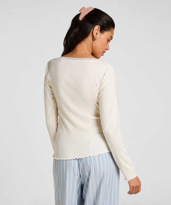 Achteraanzicht van model in crème-witte geribbelde top met lange mouwen en blauw-witte pyjamabroek.