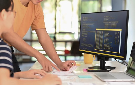 Twee personen kijken naar code op een Philips-monitor in een kantooromgeving.
