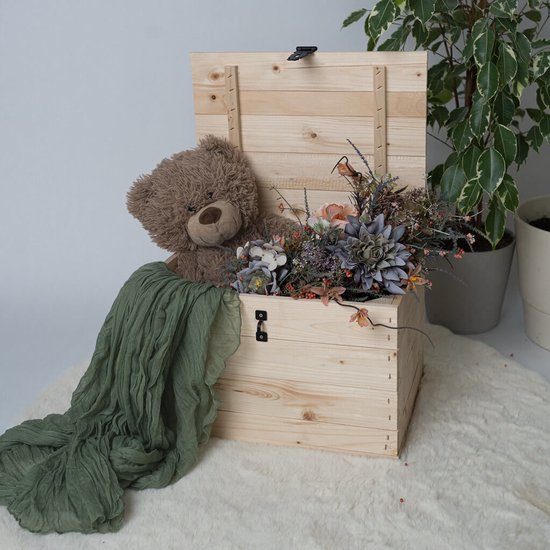 Houten kist met deksel omhoog, een bruine teddybeer, een groen stuk stof en een bos gedroogde bloemen erin.