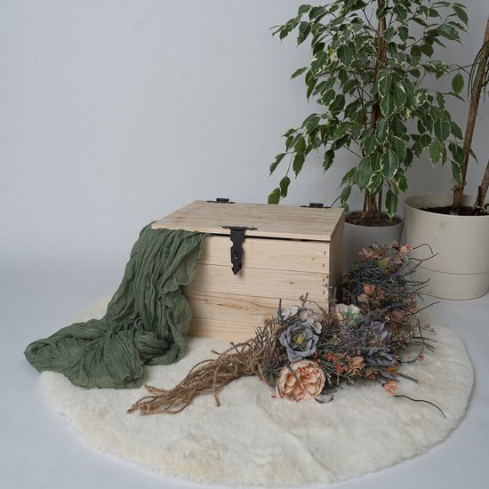 Houten kist met deksel omlaag, een groen stuk stof ernaast en een bos gedroogde bloemen op de grond.