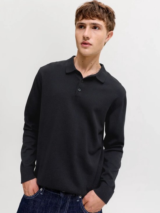 Man draagt zwart gebreid Jack & Jones poloshirt met lange mouwen, handen in zakken.