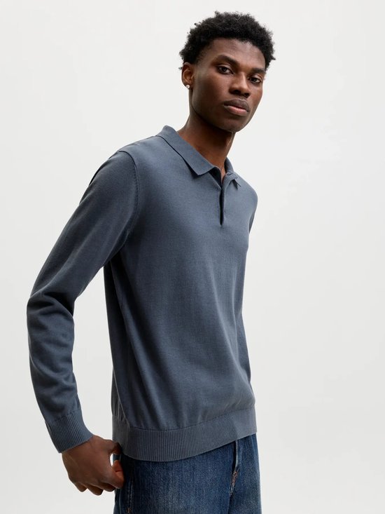 Man met donkergrijs gebreid poloshirt met lange mouwen, staand.