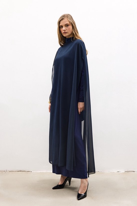 Model draagt een marineblauwe oversized maxi-tuniek van chiffon met lange mouwen en een hoge hals.