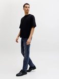 Man met een zwarte oversized t-shirt en blauwe jeans, loop van opzij.