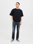 Man met donkere jeans en oversized zwart T-shirt, handen in de zakken.