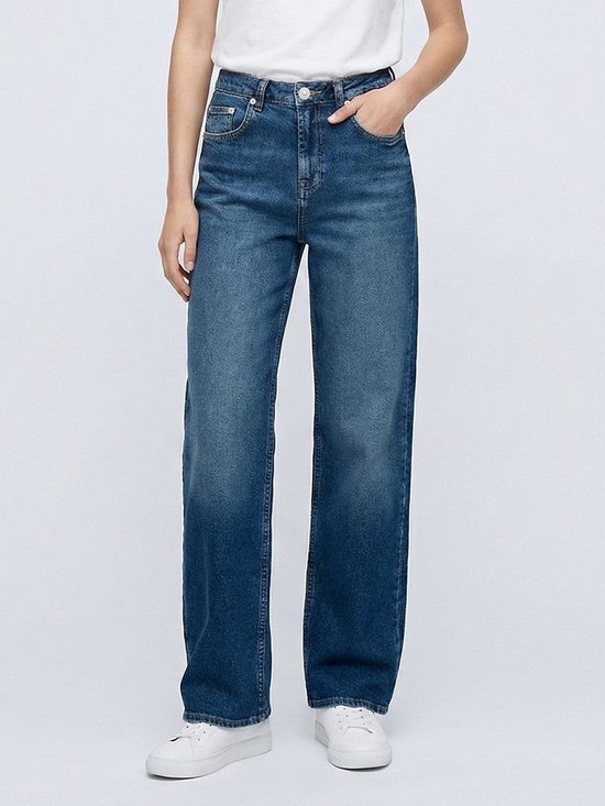 Close-up van het model in een blauwe jeans met wijde pijpen en witte sneakers.